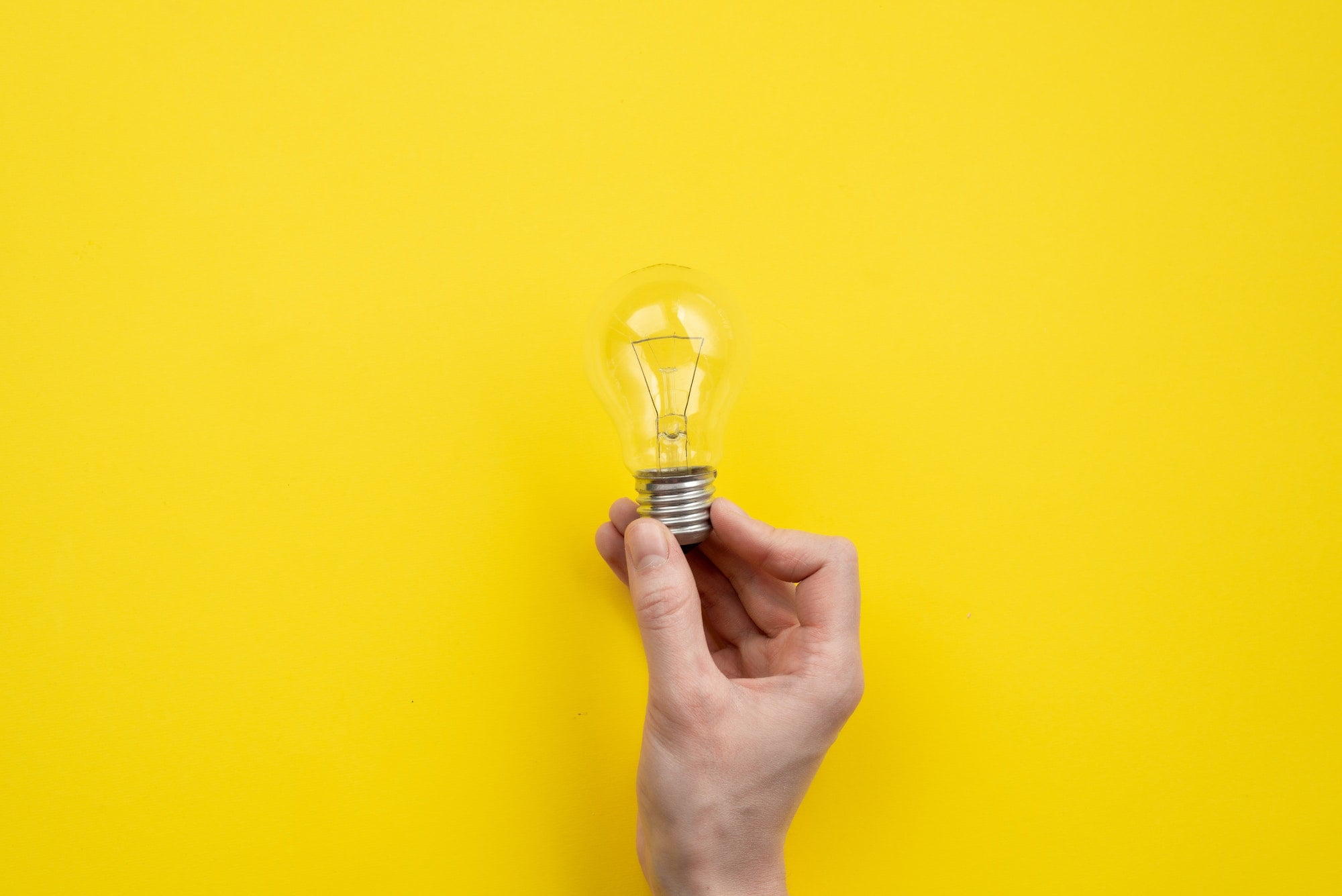Male hand holding a bulb on yellow background- Image